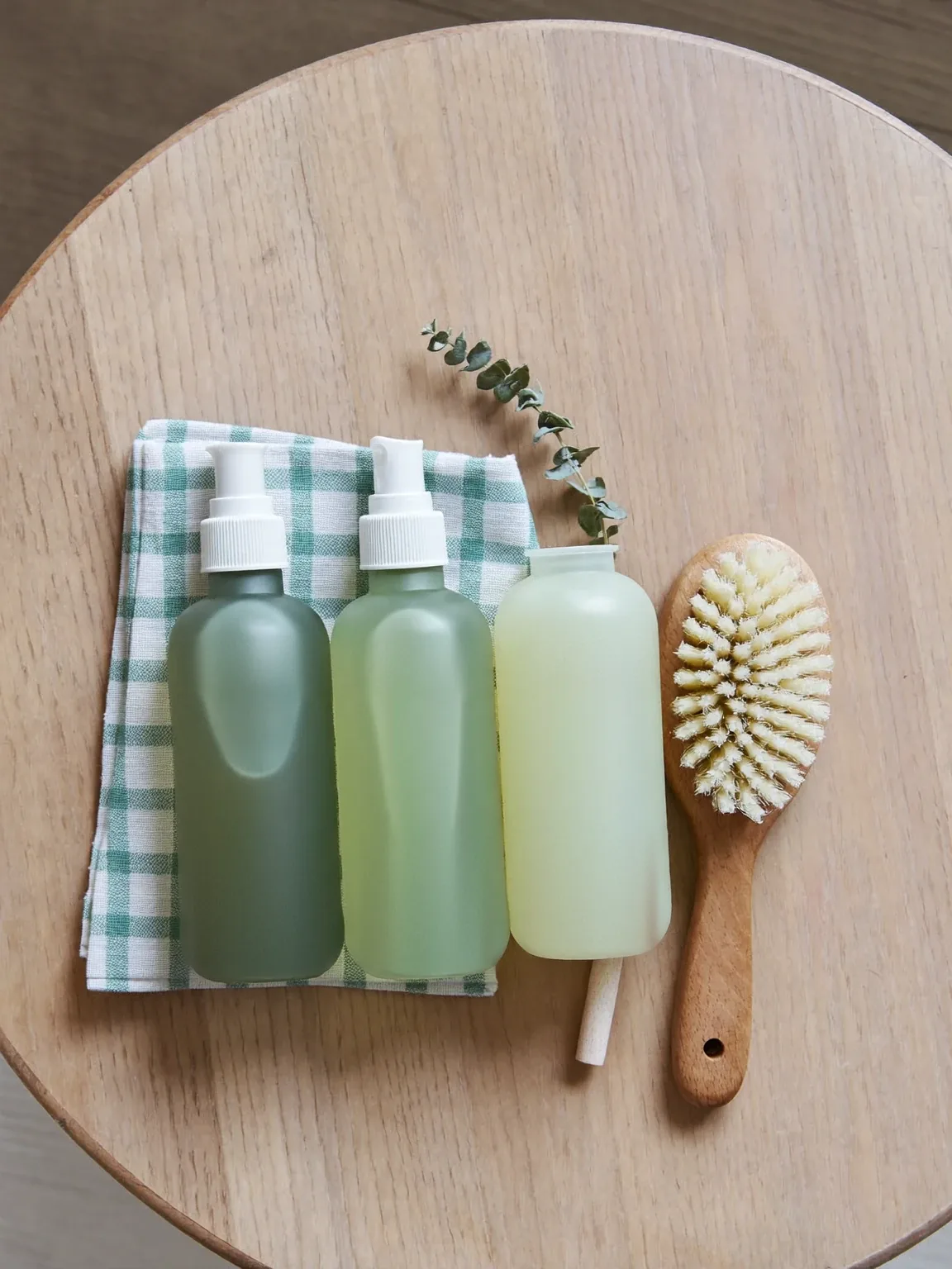 Eco-friendly cleaning bottles, a checked cloth and a wooden brush on pale oak